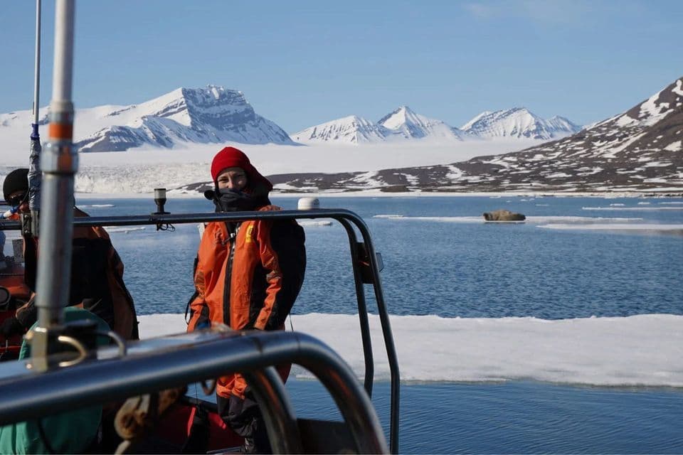 Una mujer con chaqueta naranja en un barco de un viaje en grupo de WeRoad en un mar helado con un telón de fondo de montañas nevadas.