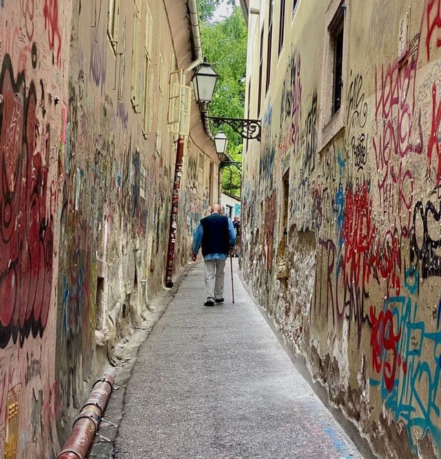 Un anciano con un bastón camina por un callejón estrecho con paredes cubiertas de coloridos grafitis.