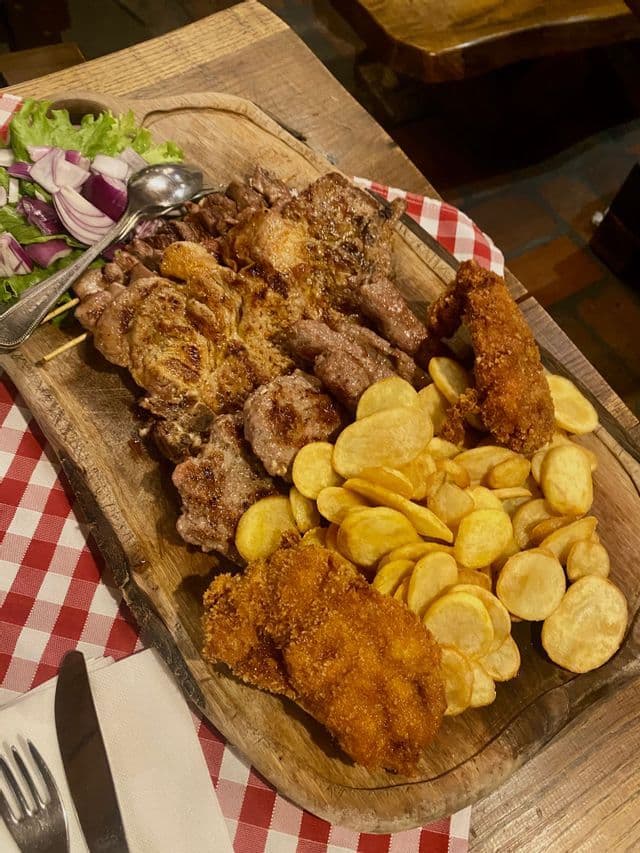 Un surtido de carnes a la parrilla, milanesas y patatas fritas, servido en una tabla de madera con ensalada.