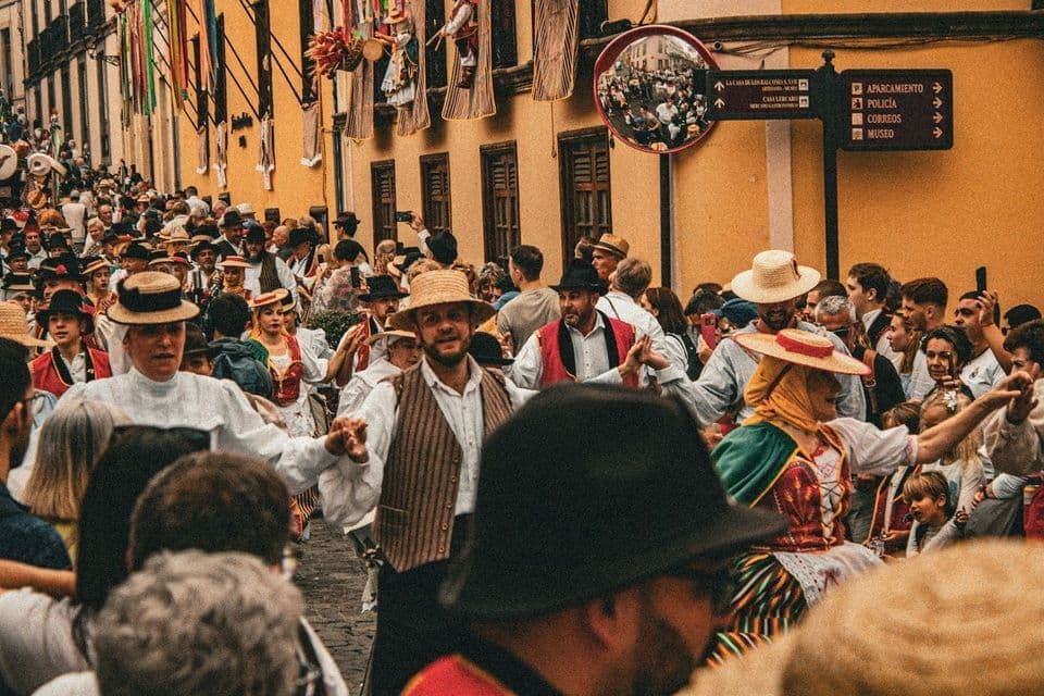 Una grande folla di persone in abiti tradizionali e cappelli di paglia che ballano in una strada stretta durante una parata festiva.