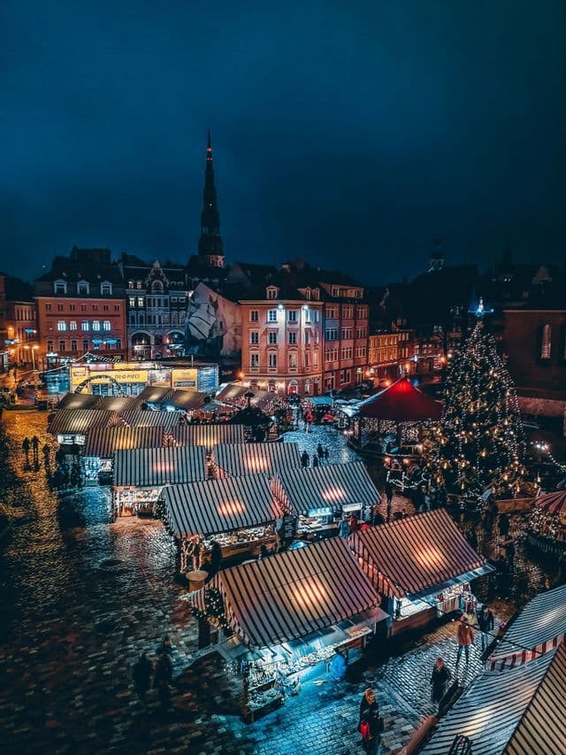 Una vista aerea di un vivace mercatino di Natale notturno, con bancarelle illuminate, un grande albero di Natale e persone in una piazza acciottolata.