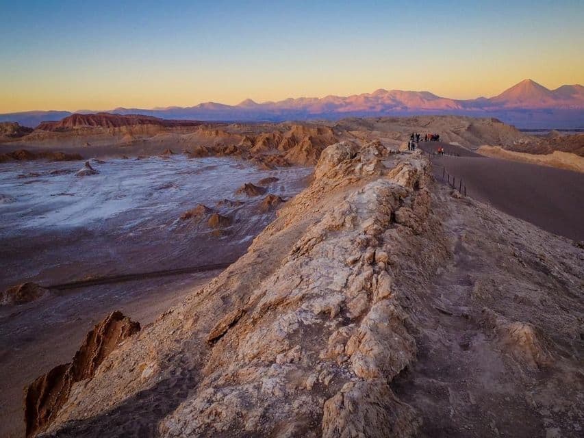 Un gruppo WeRoad si trova su una cresta rocciosa che domina una vasta valle desertica con montagne distanti al tramonto.