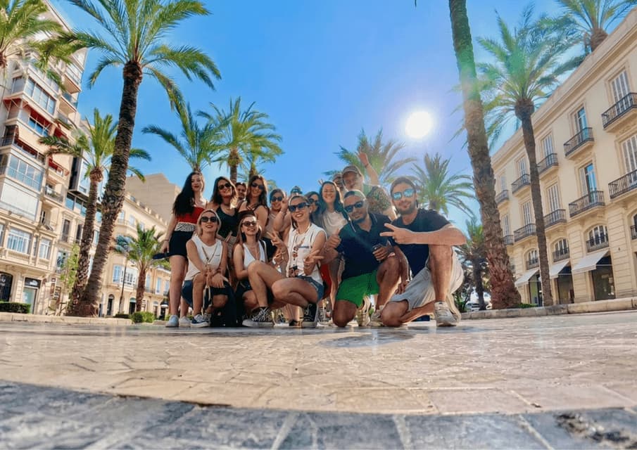 Un gruppo WeRoad si fa fotografare dal basso in una piazza assolata, circondata da alte palme ed edifici storici.