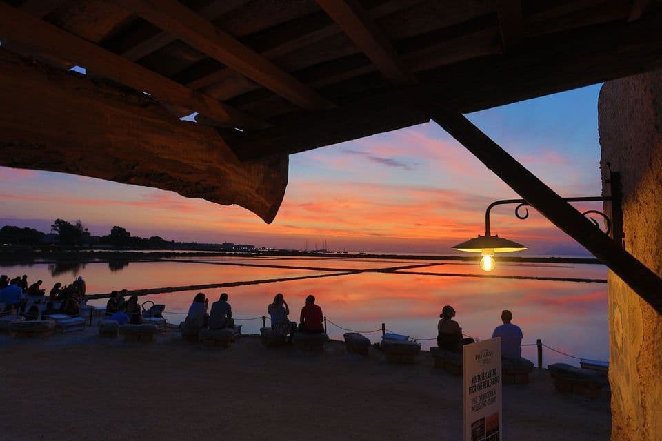 Un gruppo WeRoad osserva un tramonto colorato in riva a un'acqua calma, con il suo riflesso sulla superficie.
