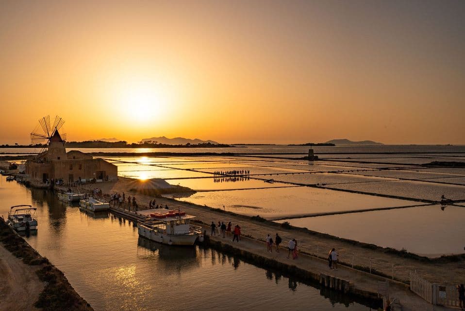 Un viaggio di gruppo WeRoad costeggia saline e un mulino a vento storico durante un tramonto dorato.