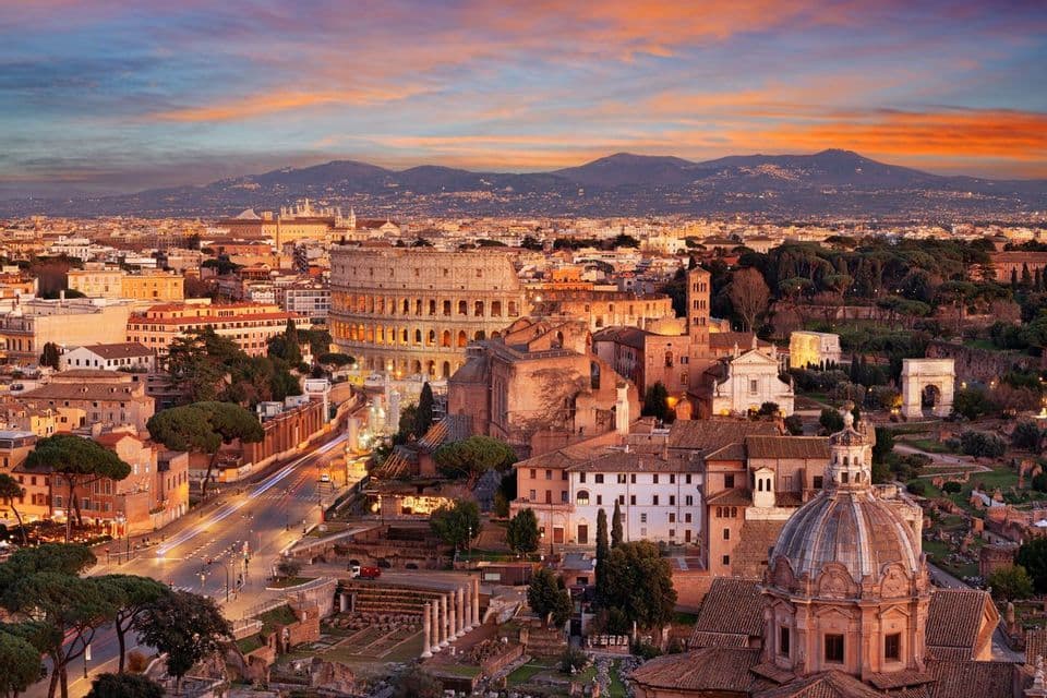 Veduta dall'alto della storica città di Roma, con il Colosseo illuminato e le antiche rovine al tramonto.