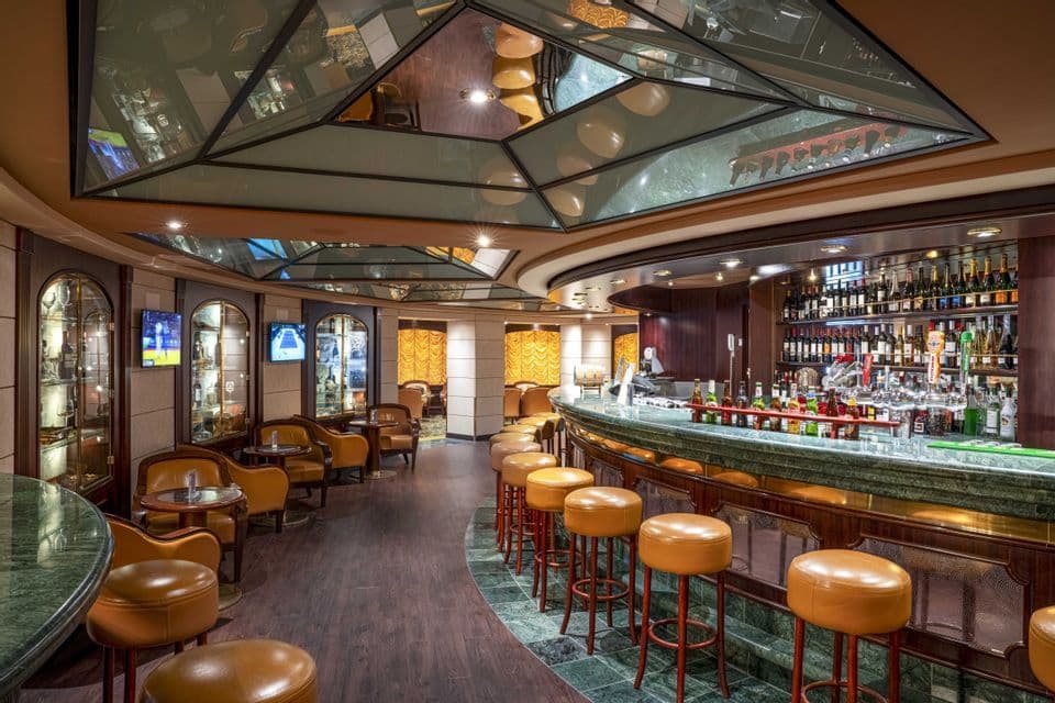 L'interno di un bar vuoto, in stile classico, con un lungo bancone curvo, sgabelli in pelle e un soffitto a specchio geometrico.