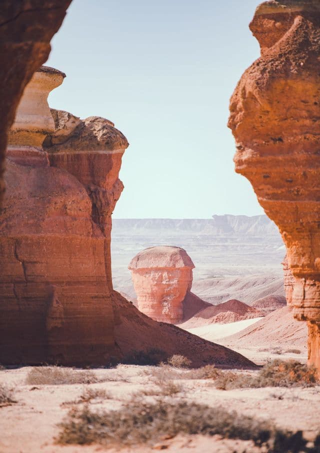 Una peculiare formazione rocciosa rossa e arrotondata si erge in una valle desertica, incorniciata da due grandi pareti di roccia.
