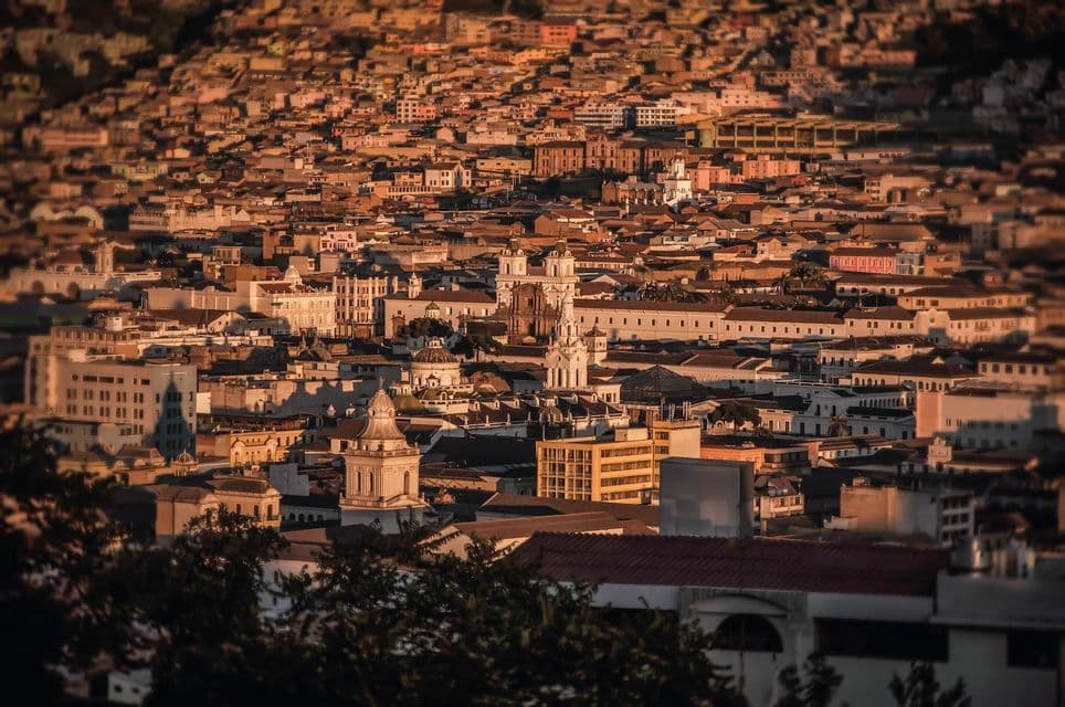 Un vaste paysage urbain de bâtiments historiques et de toits en tuiles s'étendant à flanc de colline au coucher du soleil.