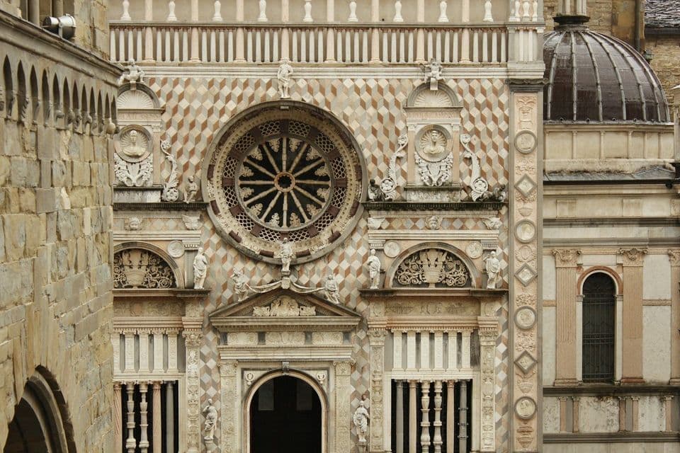 La facciata ornata di un edificio storico con un grande rosone, sculture intricate e una parete a motivi geometrici a rombi.