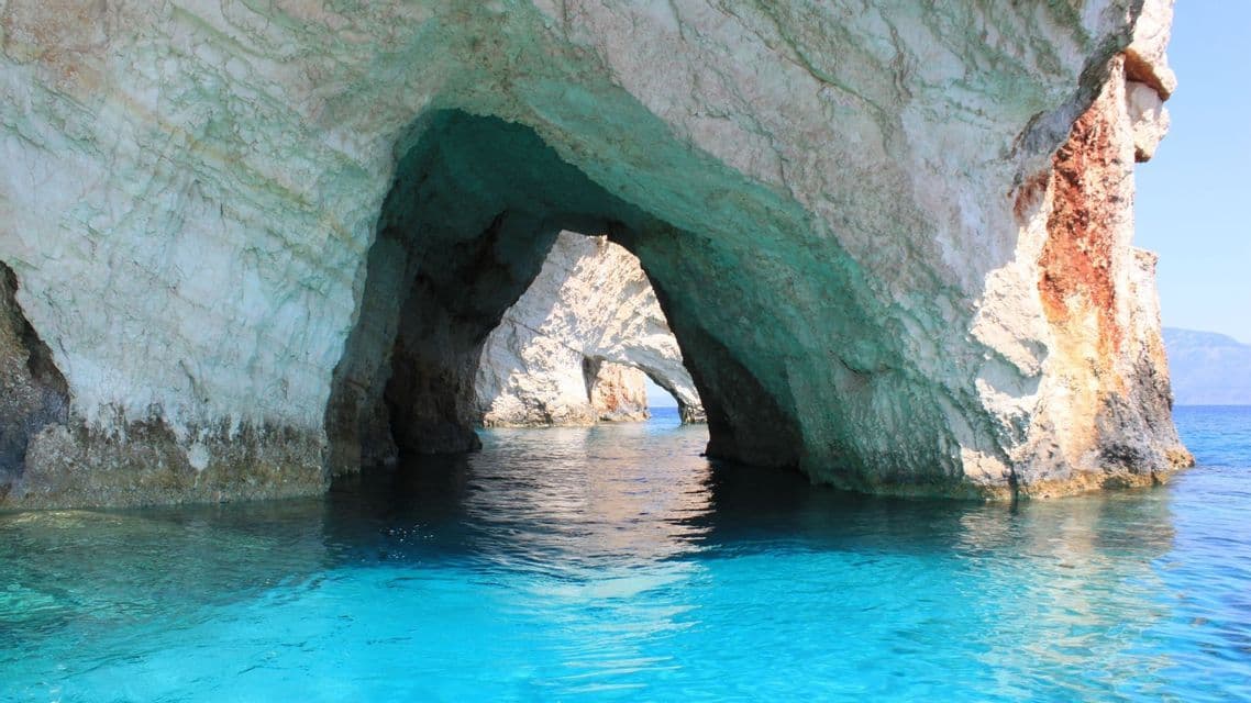 Una serie di archi di roccia bianca forma grotte marine su acque limpide e turchesi brillanti.
