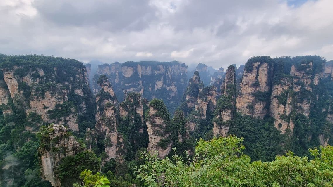 Un vasto paesaggio di imponenti formazioni rocciose a pilastro, coperte da alberi verdi e vegetazione, sotto un cielo nuvoloso.
