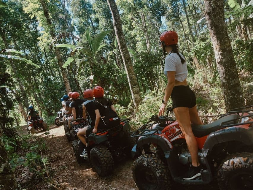 A WeRoad group trip prepares to ride quad bikes in a single file line on a trail through a dense jungle.