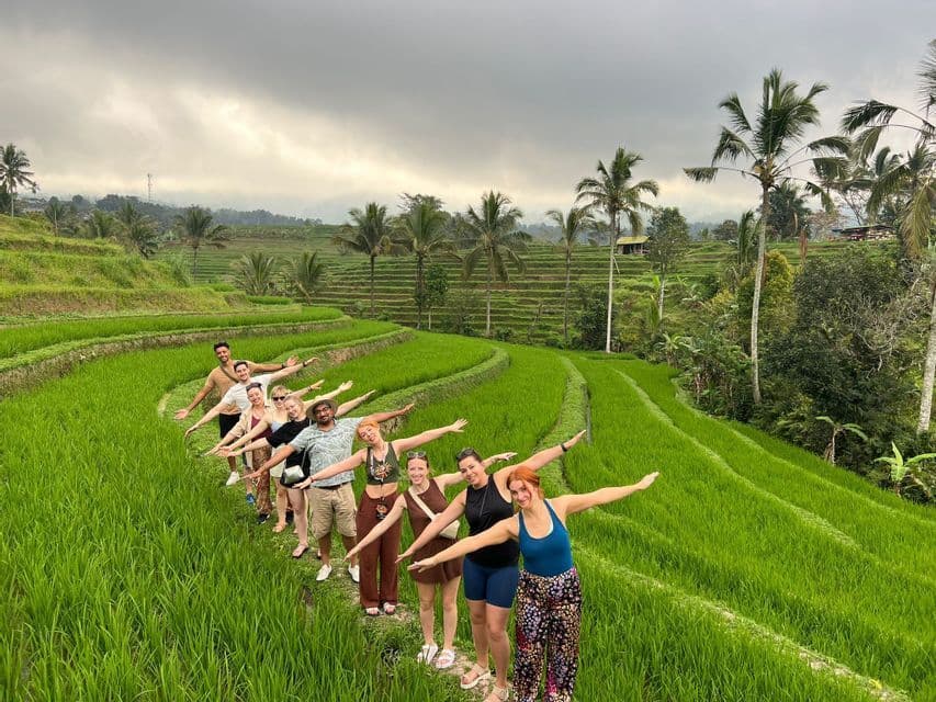 A WeRoad group trip poses in a line with arms outstretched on a path through green rice terraces.