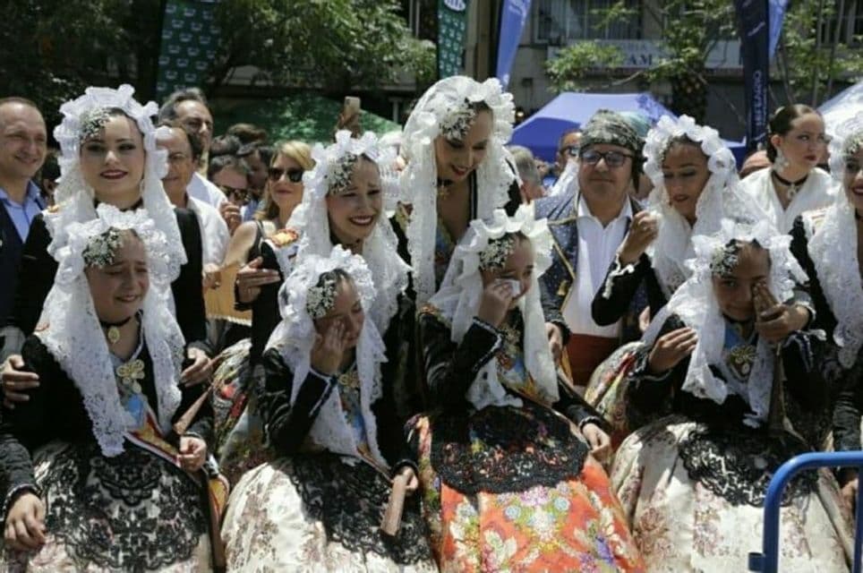 Un gruppo di donne e ragazze in abiti tradizionali con copricapi di pizzo bianco durante un festival, con alcune ragazze che appaiono emotive e piangono.