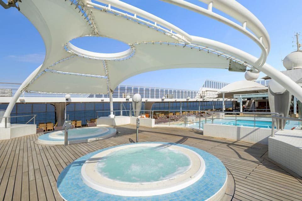 Il ponte piscina vuoto di una nave da crociera con due vasche idromassaggio sotto una grande tenda bianca in una giornata di sole.