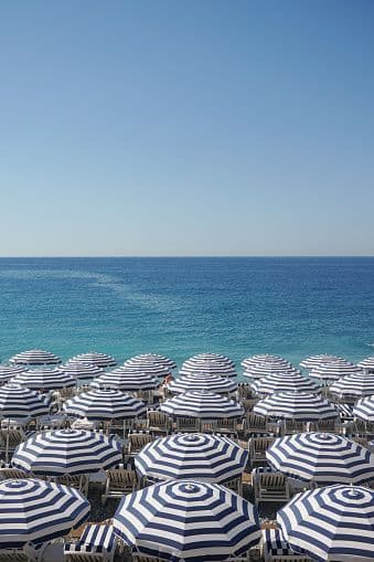 A high-angle view of rows of blue and white striped umbrellas on a beach facing the blue sea.