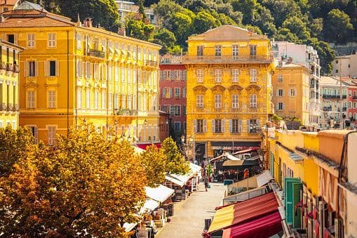 A high-angle view of a bustling street lined with yellow buildings, market stalls, and trees with autumn foliage.