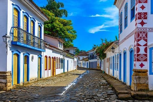 A wet cobblestone street is lined with white colonial buildings featuring colorful blue and yellow doors and windows.