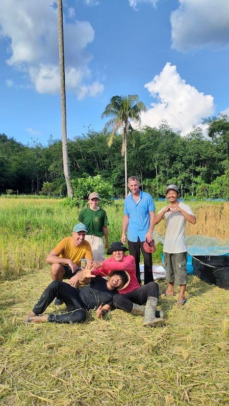Un voyage de groupe WeRoad posant pour une photo dans un champ moissonné, avec des palmiers et une forêt en arrière-plan.