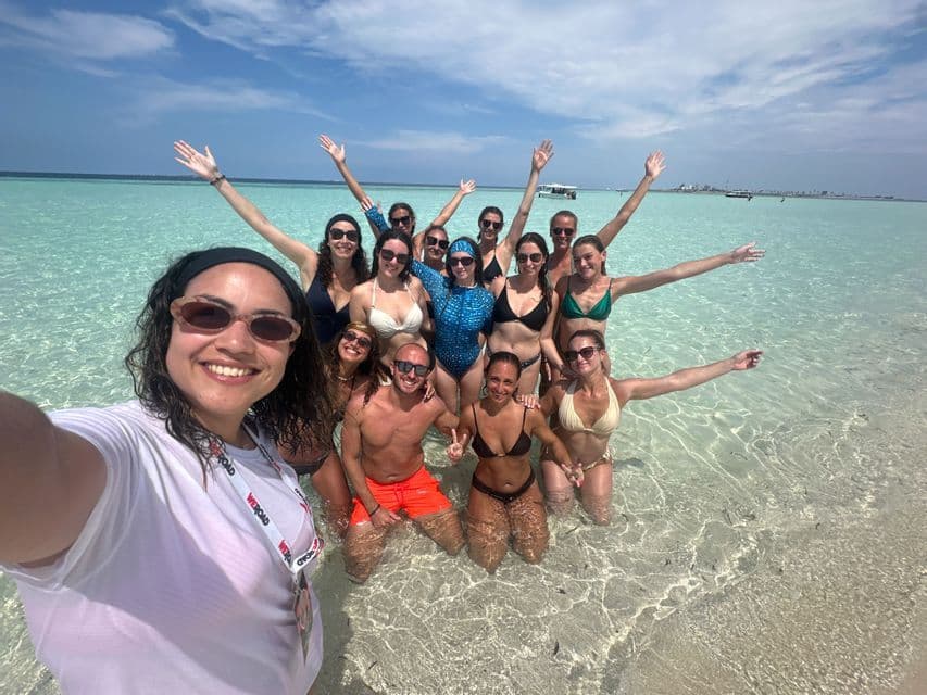 Eine WeRoad-Reisegruppe macht ein Selfie und posiert dabei an einem sonnigen Tag im seichten, klaren türkisfarbenen Wasser.