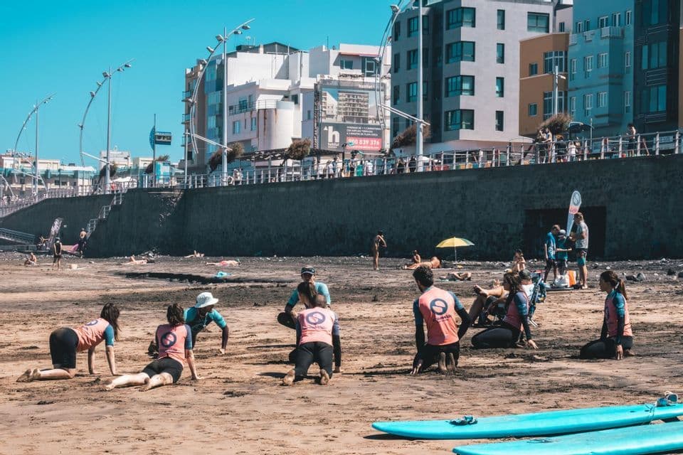 Un viaggio di gruppo WeRoad si prepara su una spiaggia sabbiosa per una lezione di surf, con le tavole da surf in primo piano.