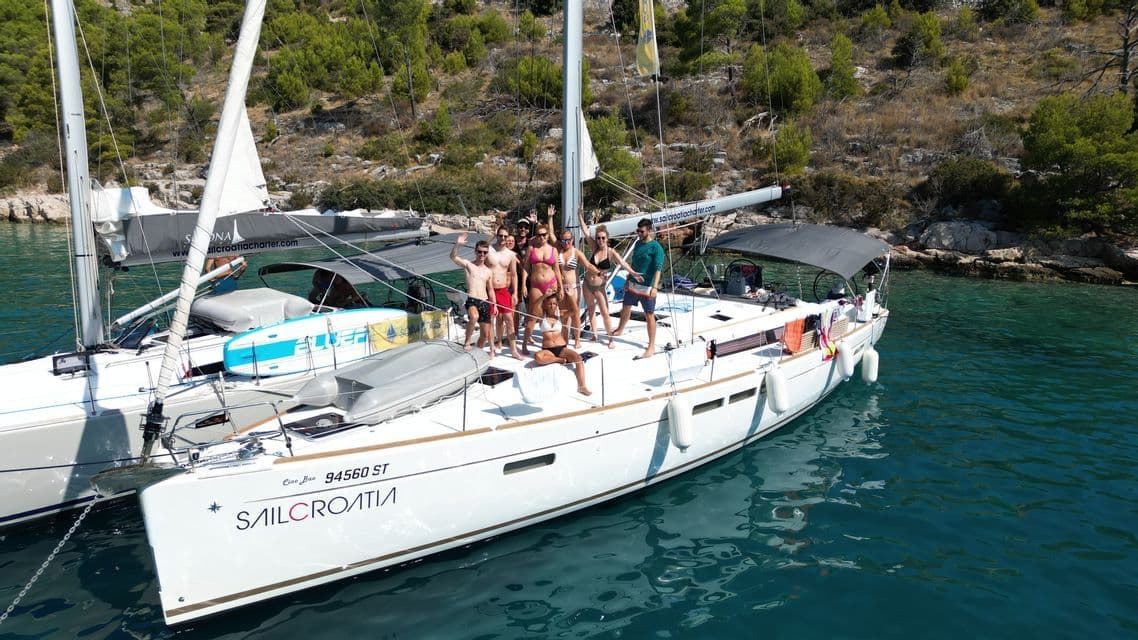 Luftaufnahme einer WeRoad-Gruppe, die auf dem Deck eines Segelbootes in einer türkisfarbenen Bucht posiert und lächelt.