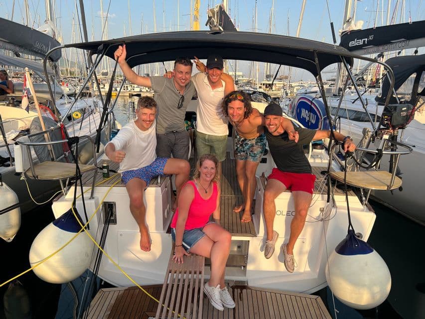 Eine WeRoad-Gruppe von sieben Personen lächelt und posiert am Heck eines Segelbootes, das in einem Yachthafen liegt.