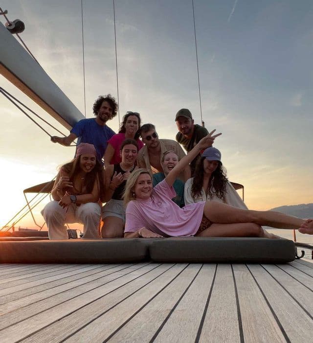 Eine WeRoad-Gruppenreise mit lächelnden und posierenden Menschen auf dem Holzdeck eines Bootes bei Sonnenuntergang.