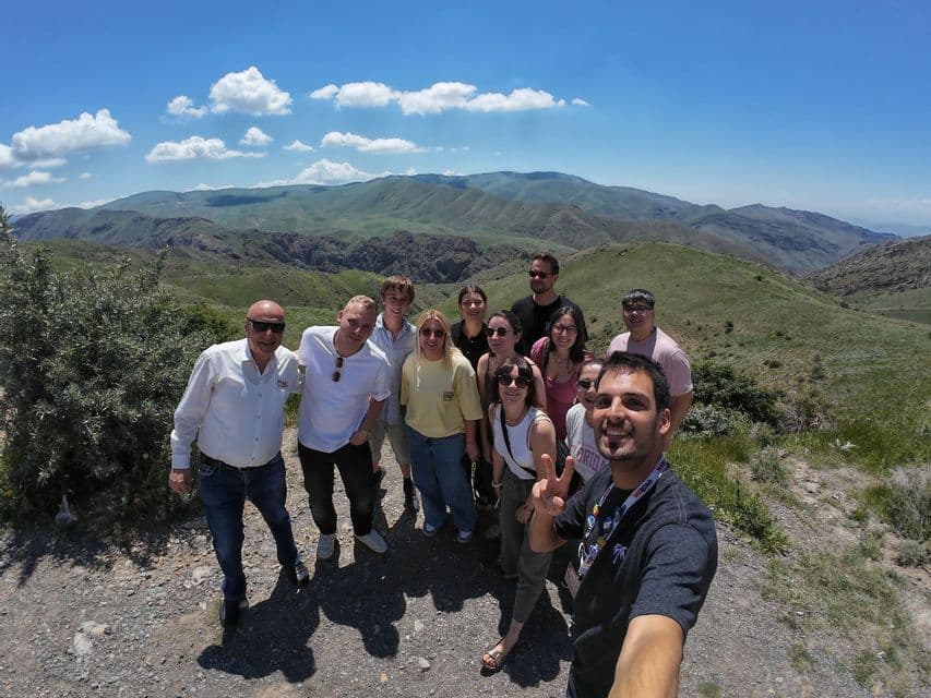 Eine WeRoad-Gruppe macht ein Selfie auf einem Berg-Aussichtspunkt mit einer weiten Landschaft aus grünen, sanften Hügeln im Hintergrund.