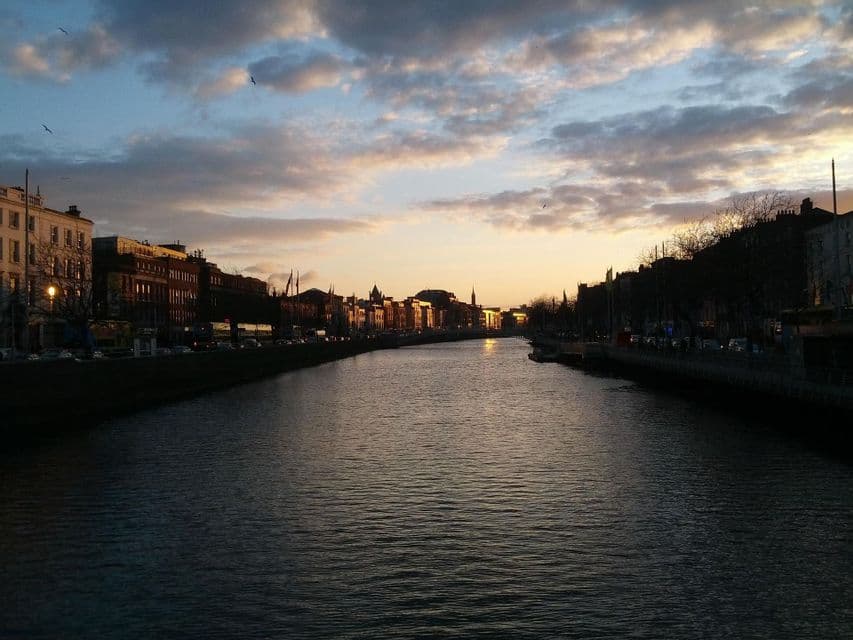 Un ampio fiume attraversa una città al tramonto, con edifici che costeggiano le rive sotto un cielo nuvoloso.