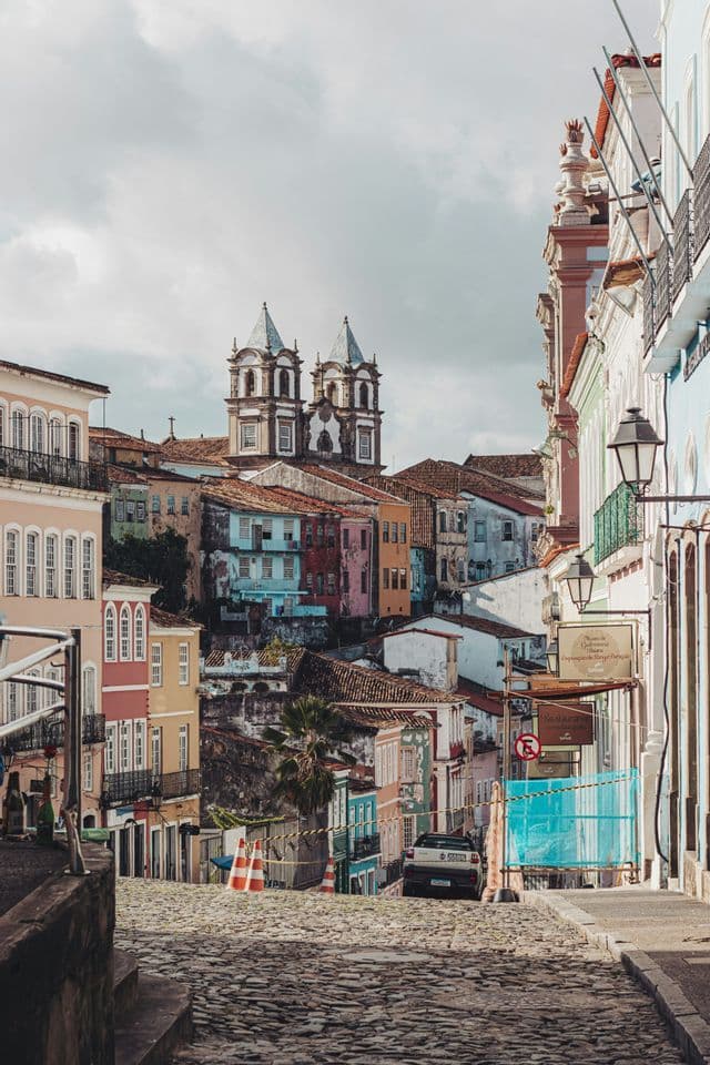 Una vista lungo una ripida strada acciottolata fiancheggiata da colorati edifici storici, con una chiesa a doppia torre visibile in lontananza.