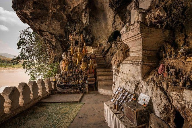 Molte statue di Buddha dorate fiancheggiano una scalinata di pietra all'interno di un santuario rupestre che si affaccia su un ampio fiume.