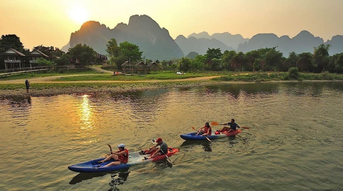 Un gruppo WeRoad in kayak su un fiume al tramonto, con grandi montagne in silhouette sullo sfondo.