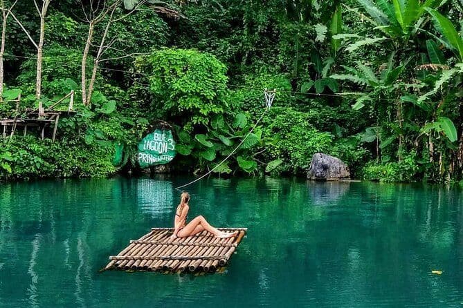 Una donna in bikini siede su una zattera di bambù che galleggia su una laguna turchese circondata da una fitta giungla verde.