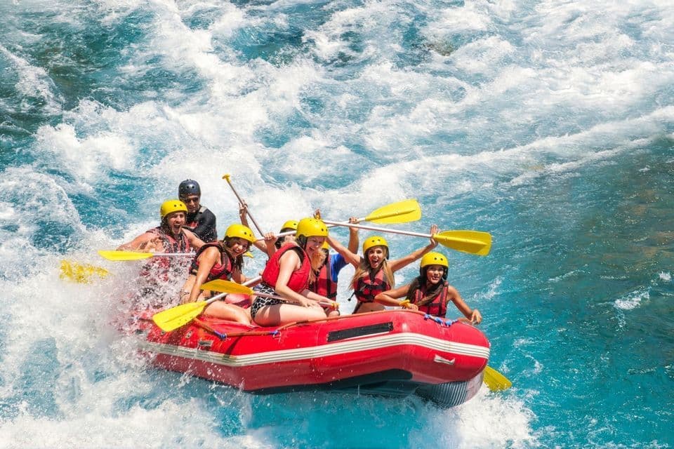 Eine WeRoad Gruppenreise jubelt beim Wildwasser-Rafting in einem roten Schlauchboot auf turbulentem blauem Wasser.