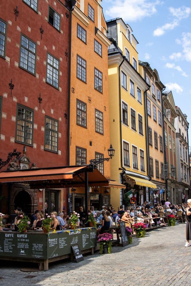 Patrons dining at an outdoor cafe on a cobblestone street lined with colorful historic buildings.