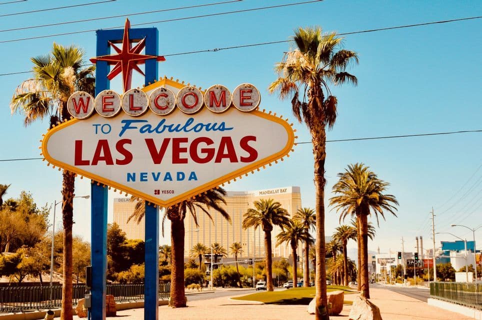 El cartel de Bienvenidos a Las Vegas fabuloso en una carretera bordeada de palmeras bajo un cielo azul despejado