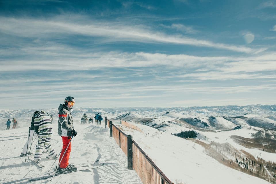 Un viaje en grupo de esquiadores de WeRoad se detiene en una cresta nevada de la montaña, contemplando una vasta cordillera bajo un cielo parcialmente nublado.