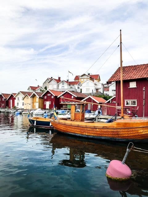 Wooden boats are docked in a calm harbor in front of a village with colorful red and white houses on a hillside.