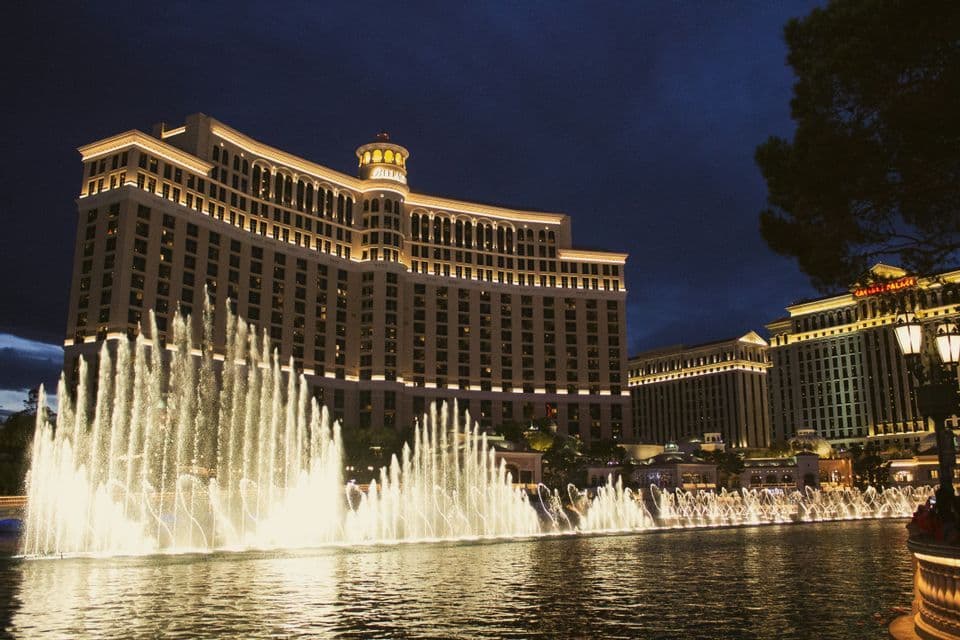 Fuentes iluminadas actúan en un gran lago frente a un gran hotel de varios pisos por la noche.