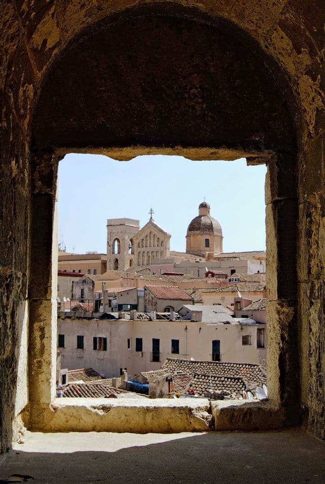 A view of a historic city's rooftops, a church tower, and a dome, framed by a weathered stone archway.