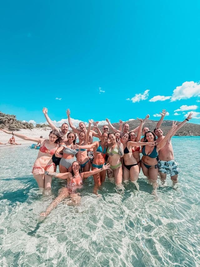 A WeRoad group trip in swimwear smiles and poses together while standing in clear, shallow sea water.