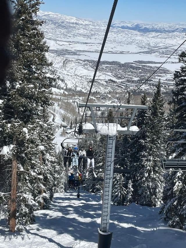 Un viaje en grupo de WeRoad en telesilla por una montaña nevada, con un vasto valle nevado y pinos abajo.