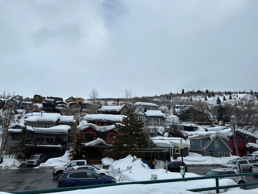 Un pueblo en la ladera con casas coloridas y calles cubiertas de una espesa capa de nieve bajo un cielo nublado.