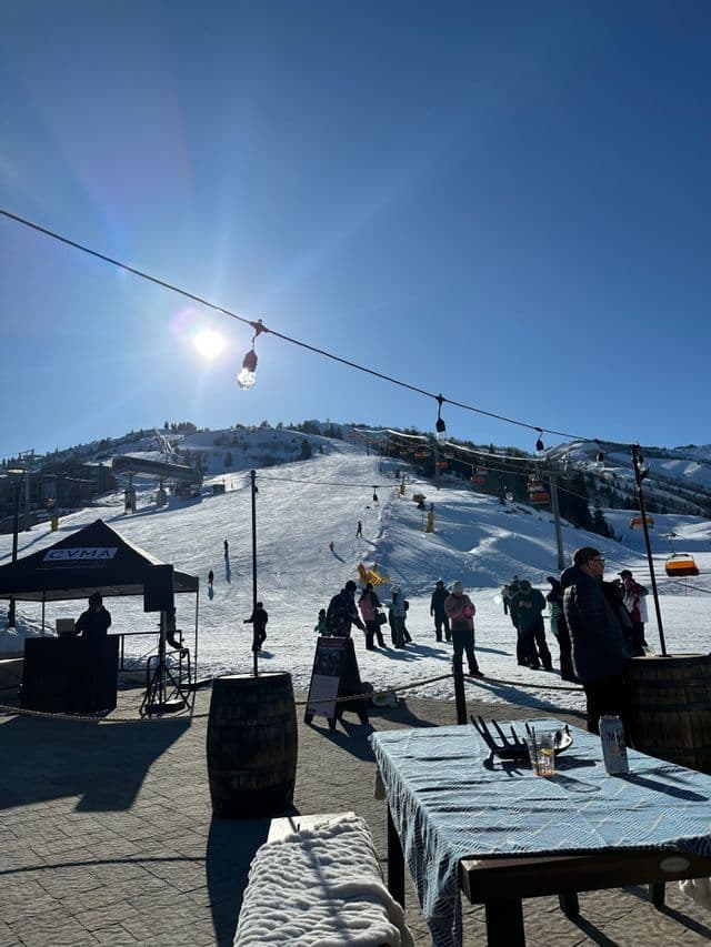 Una terraza soleada al aire libre en una estación de esquí, con personas observando a los esquiadores en las pistas de nieve.
