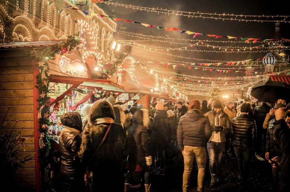 Una folla esplora un vivace mercato festivo all'aperto di notte, illuminato da lucine e bandiere colorate.