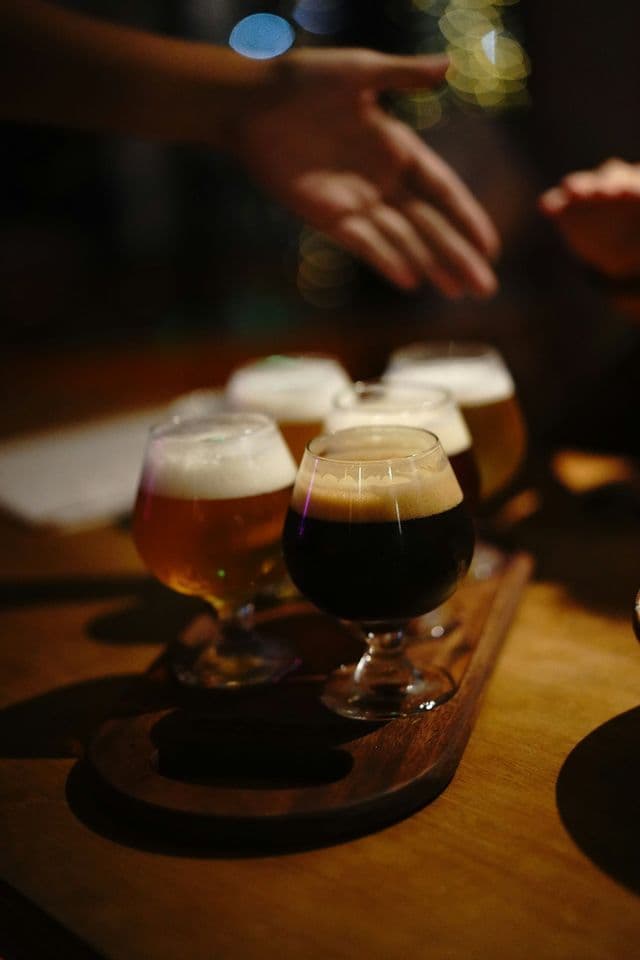 Primo piano di un flight di degustazione di birra artigianale con cinque birre diverse in bicchieri su una paletta di legno.