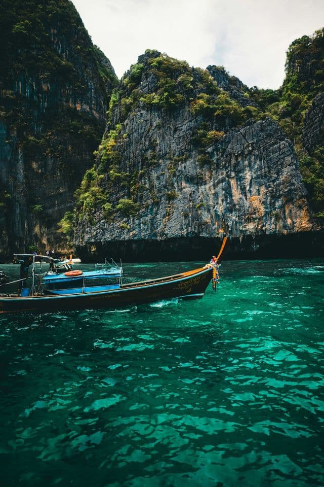 Una tradizionale barca a coda lunga naviga su acque turchesi accanto a grandi scogliere rocciose ricoperte di vegetazione verde.
