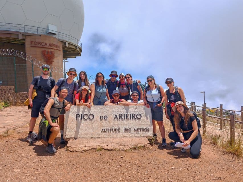 Un gruppo WeRoad di escursionisti in posa per una foto di gruppo intorno a un cartello in pietra su una cima di montagna, con una cupola radar sullo sfondo.